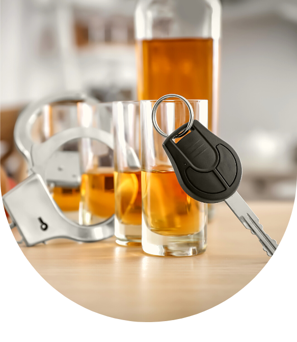 Glasses of alcohol with handcuffs and car key on wooden table.